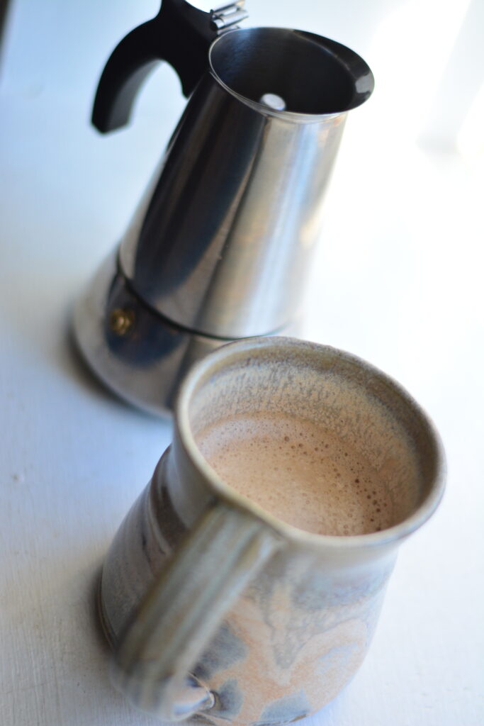 Stovetop espresso maker with hot latte in mug