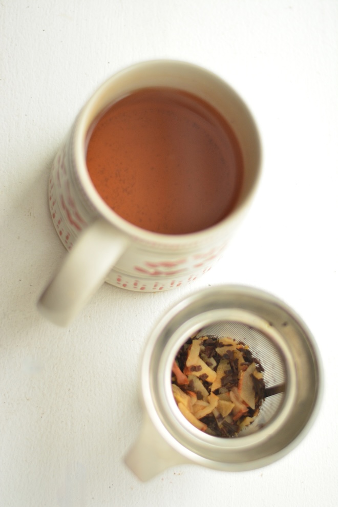 loose leaf ginger tea in strainer beside mug of hot ginger tea