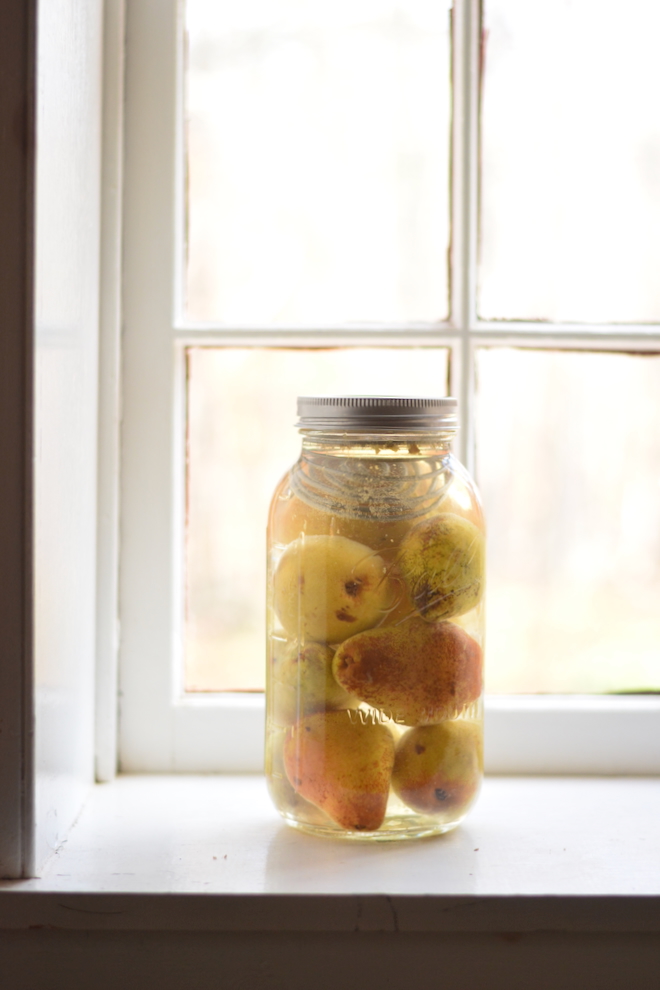 half gallon mason jar filled with fermenting pears sitting on kitchen window ledge