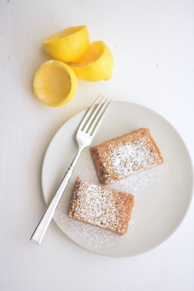 fresh squeezed lemons and a plate of einkorn lemon bars dusted with confectioners sugar
