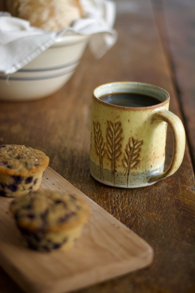 hot vanilla colostrum latte in a mug with blueberry muffins nearby