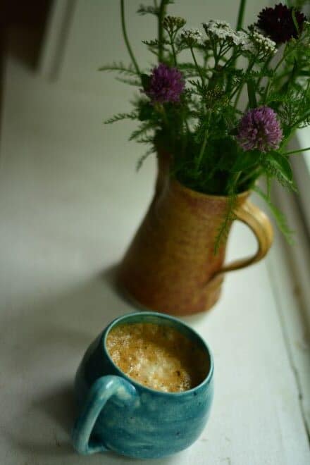hot vanilla colostrum latte in a mug with flowers in vase