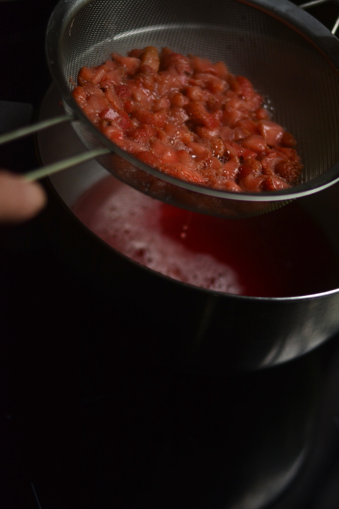 straining out cooked strawberries when making homemade strawberry syrup