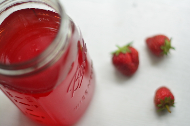 deep red syrup in mason jar with strawberries laying beside it