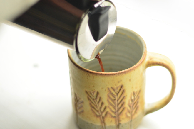 a moka pot is pouring espresso into a yellow pottery mug