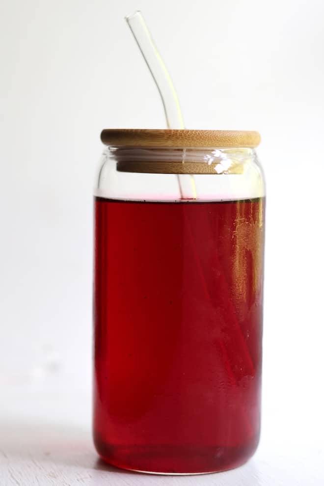a glass of deep red tea with a wooden lid and straw