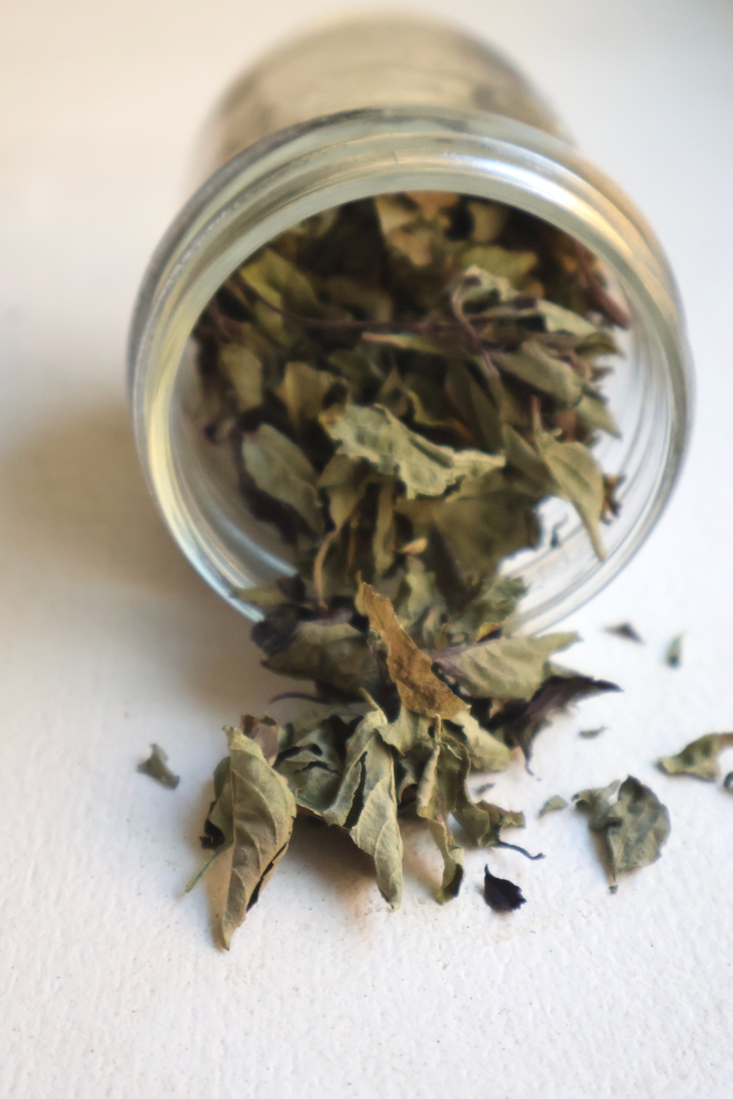 glass jar of dried basil leaves pouring onto white table