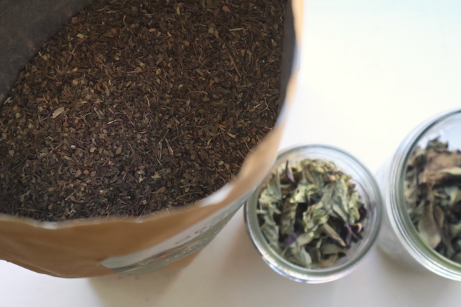 a bag of finely crushed, dry Tulsi basil leaves beside two jars of whole leaves 