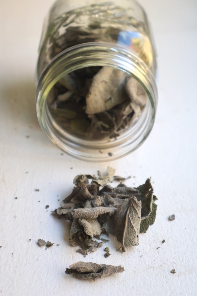 dried sage leaves pouring out of glass jar onto table