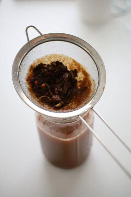 straining pumpkin and loose leaf chai tea from chai concentrate into a jar