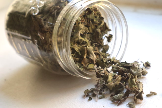 dried oregano leaves spilling out of mason jar onto white table 